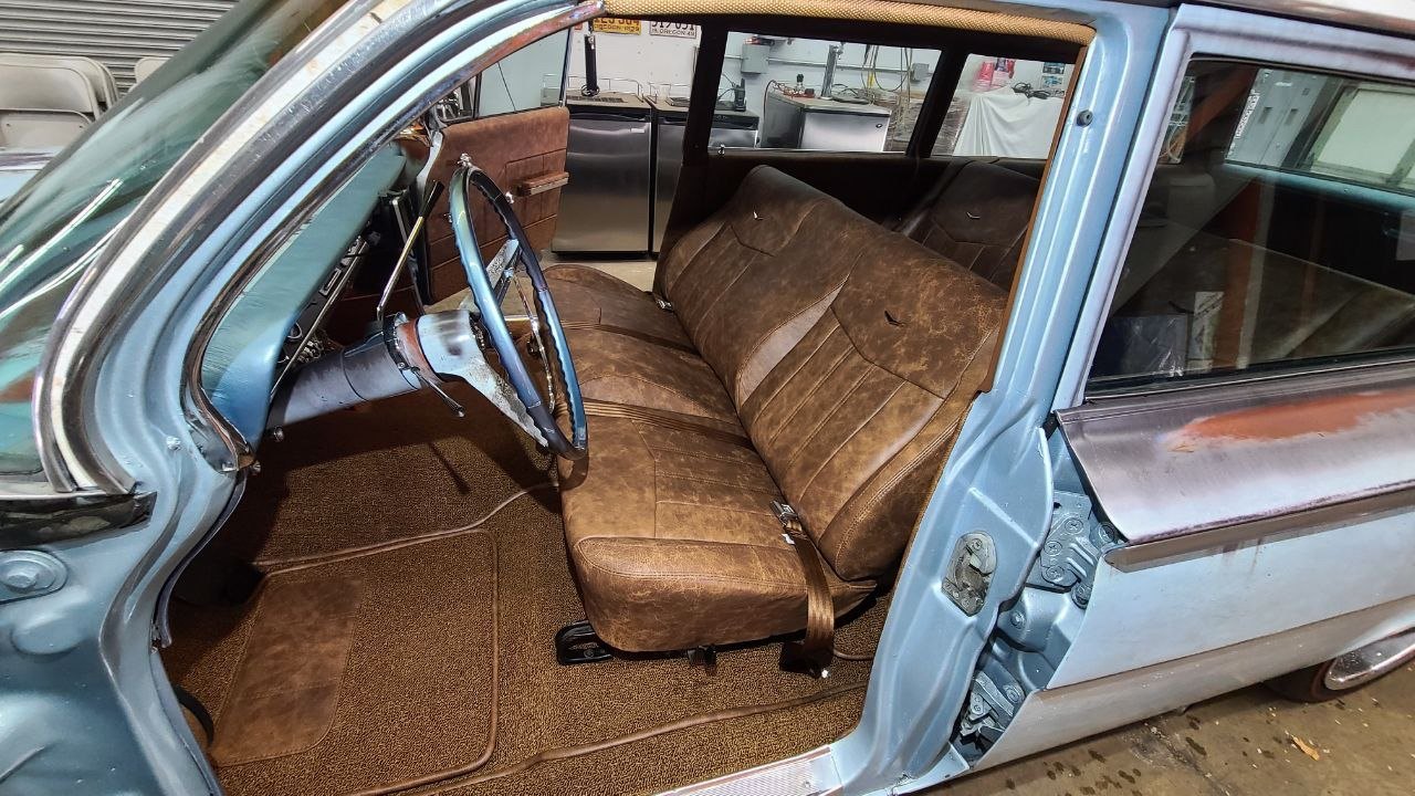 Front bench in distressed brown leather with matching door panel and carpet, seen from the driver door of a patina blue station wagon